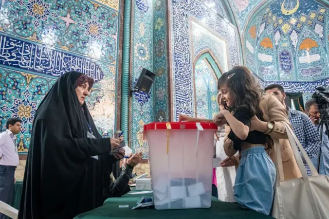 Annesinin kucağında taşıdığı küçük bir kız çocuğu, Tahran'daki bir seçim merkezinde annesinin oyunu kullanıyor. Masanın karşısında, mozaik kaplı duvarların önünde, siyah çarşaf giymiş bir kadın onları izliyor.