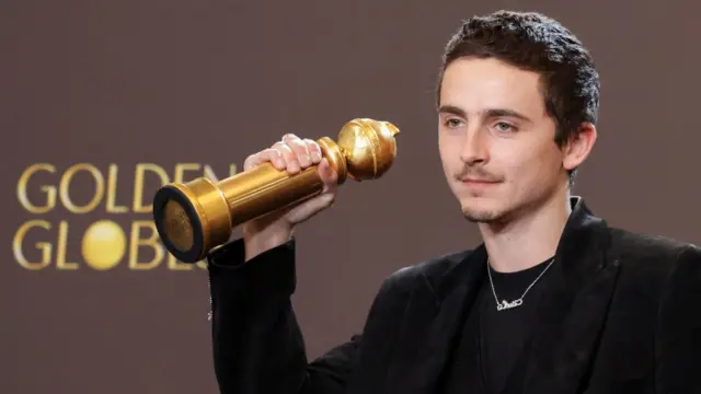 Chalamet Altın Küre ödülünü tutuyor. Siyah bir ceket ve tişört giymiş.